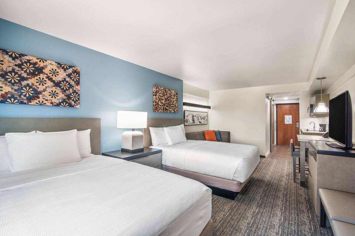 Een hotelkamer met twee bedden, een bureau, een televisie en kunstwerken aan de muur.