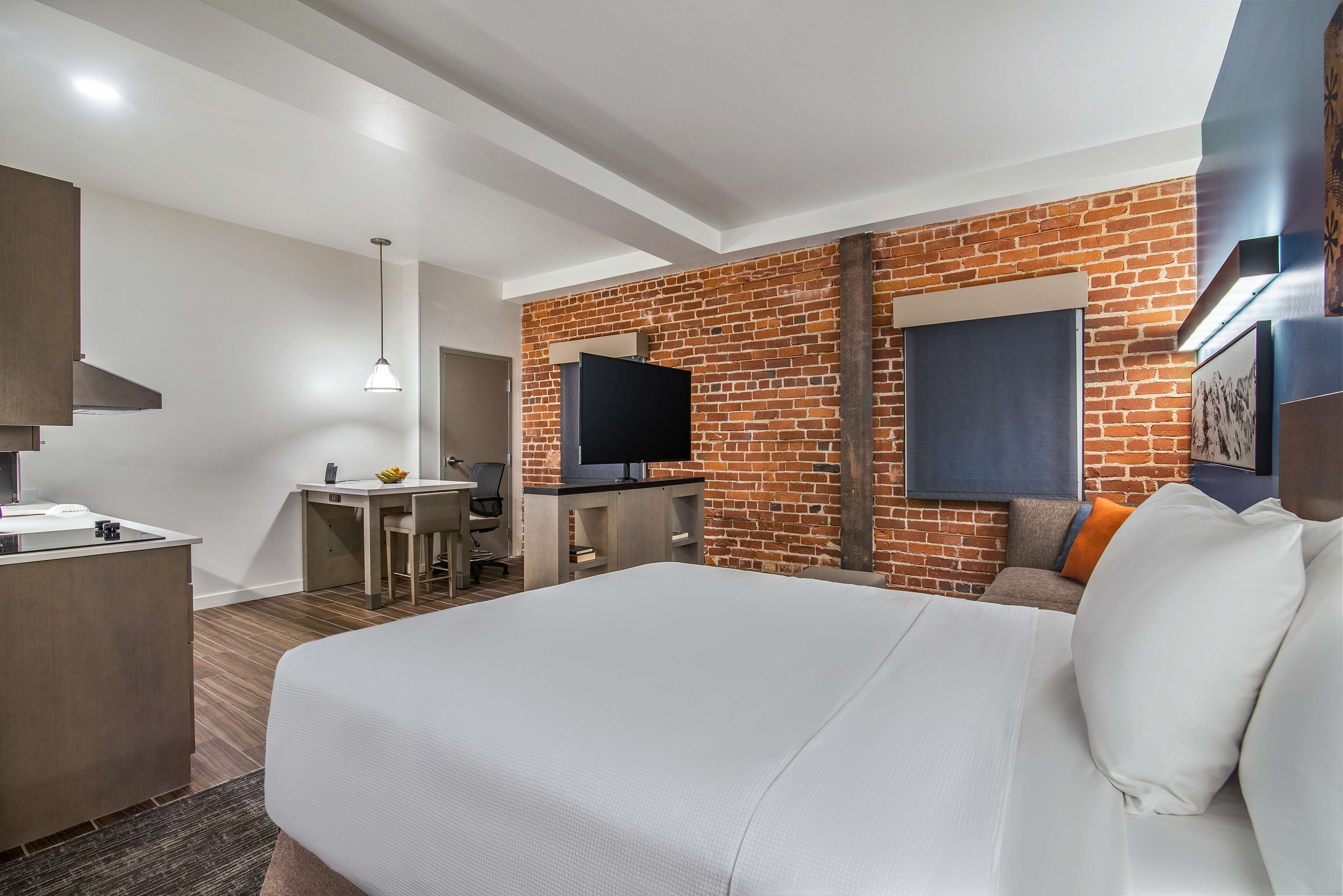 A hotel room with a large bed, a desk with a chair, a television, and a brick wall.