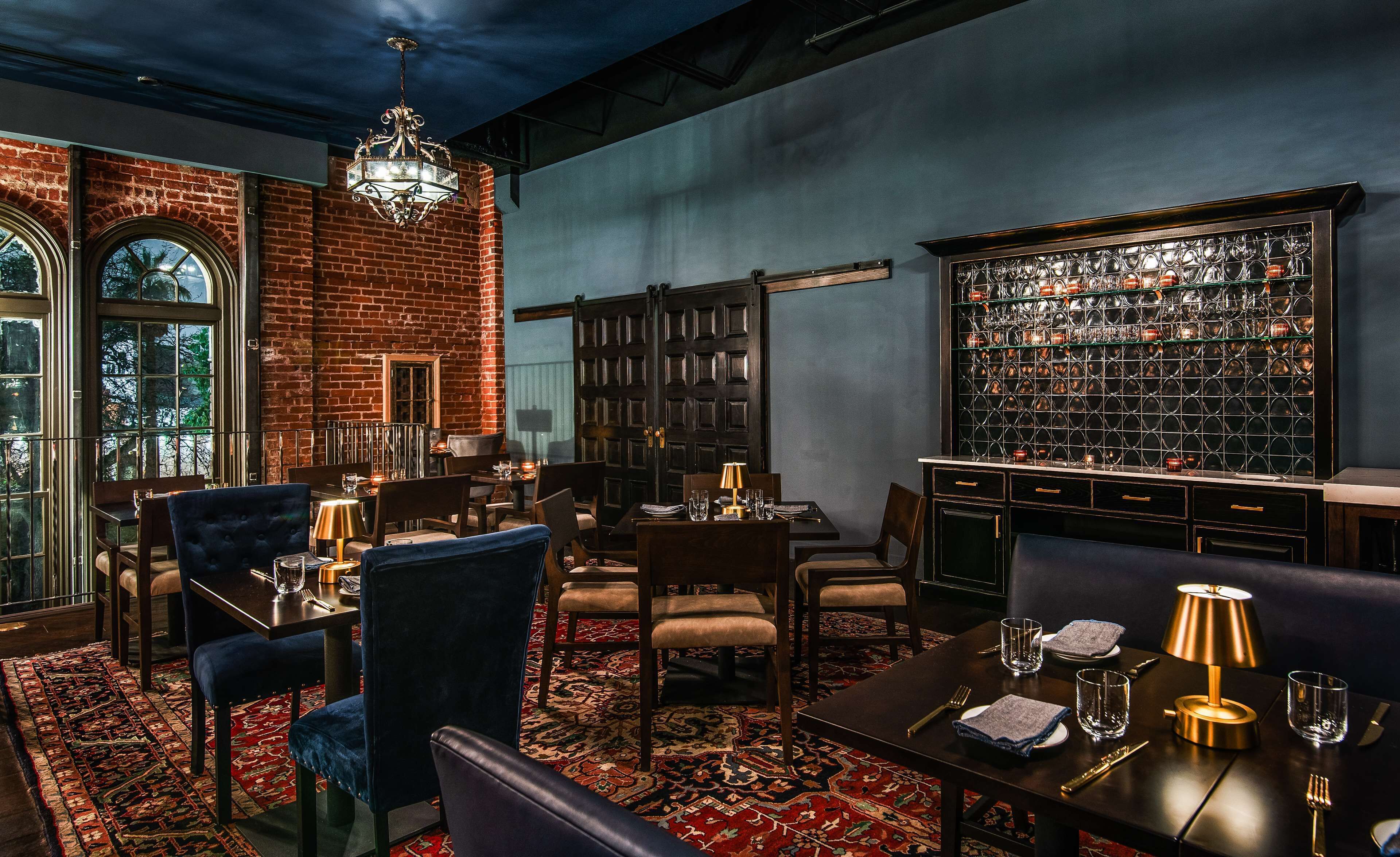 Una habitación tenuemente iluminada con pared de ladrillo, un candelabro, una estantería y una mesa dispuesta para comer.