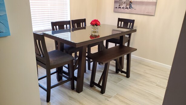 Una mesa de comedor con cuatro sillas, un jarrón con flores rojas y un cuadro en la pared.