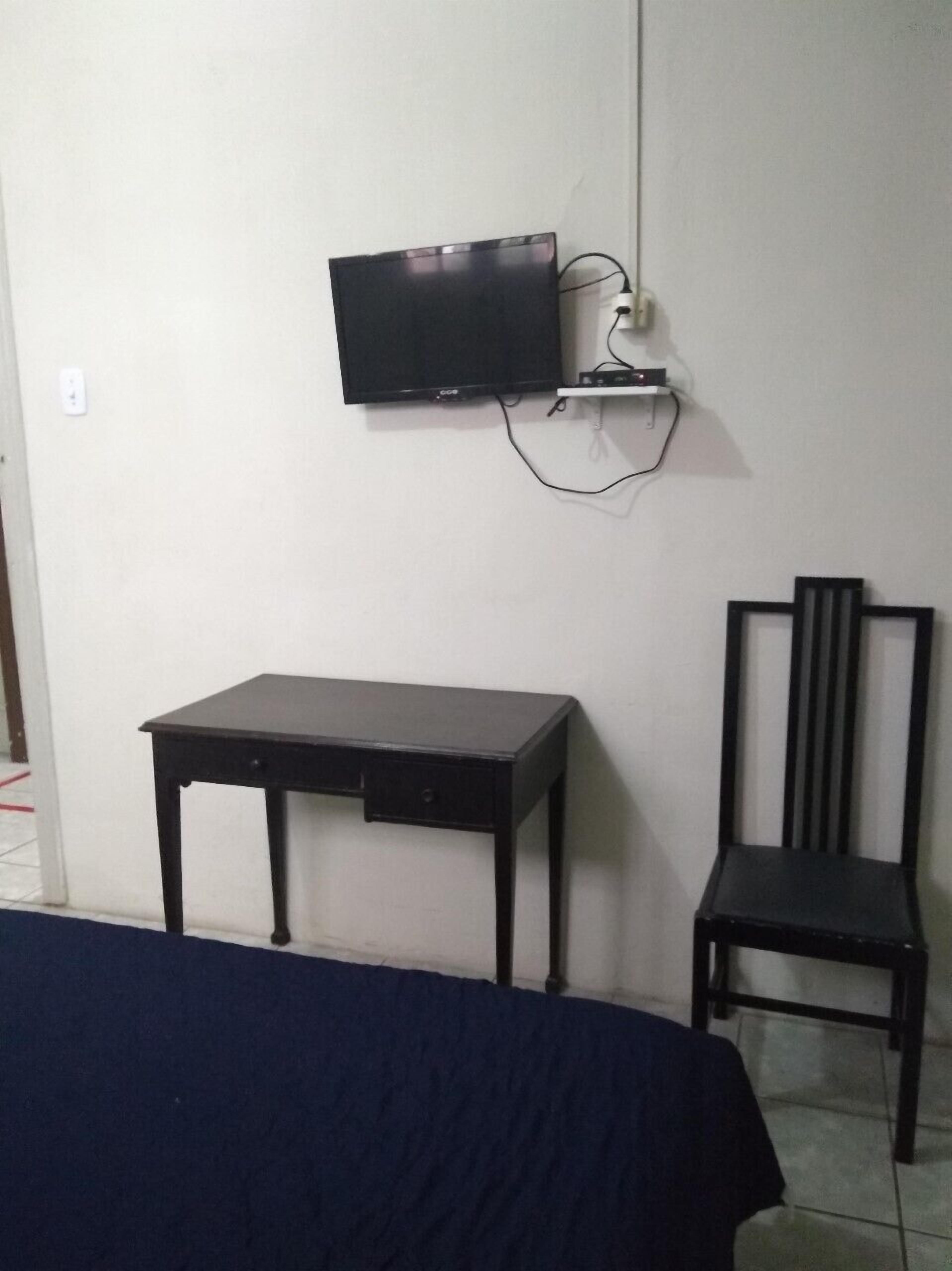 A room with a bed, a desk, a chair, and a television mounted on the wall.