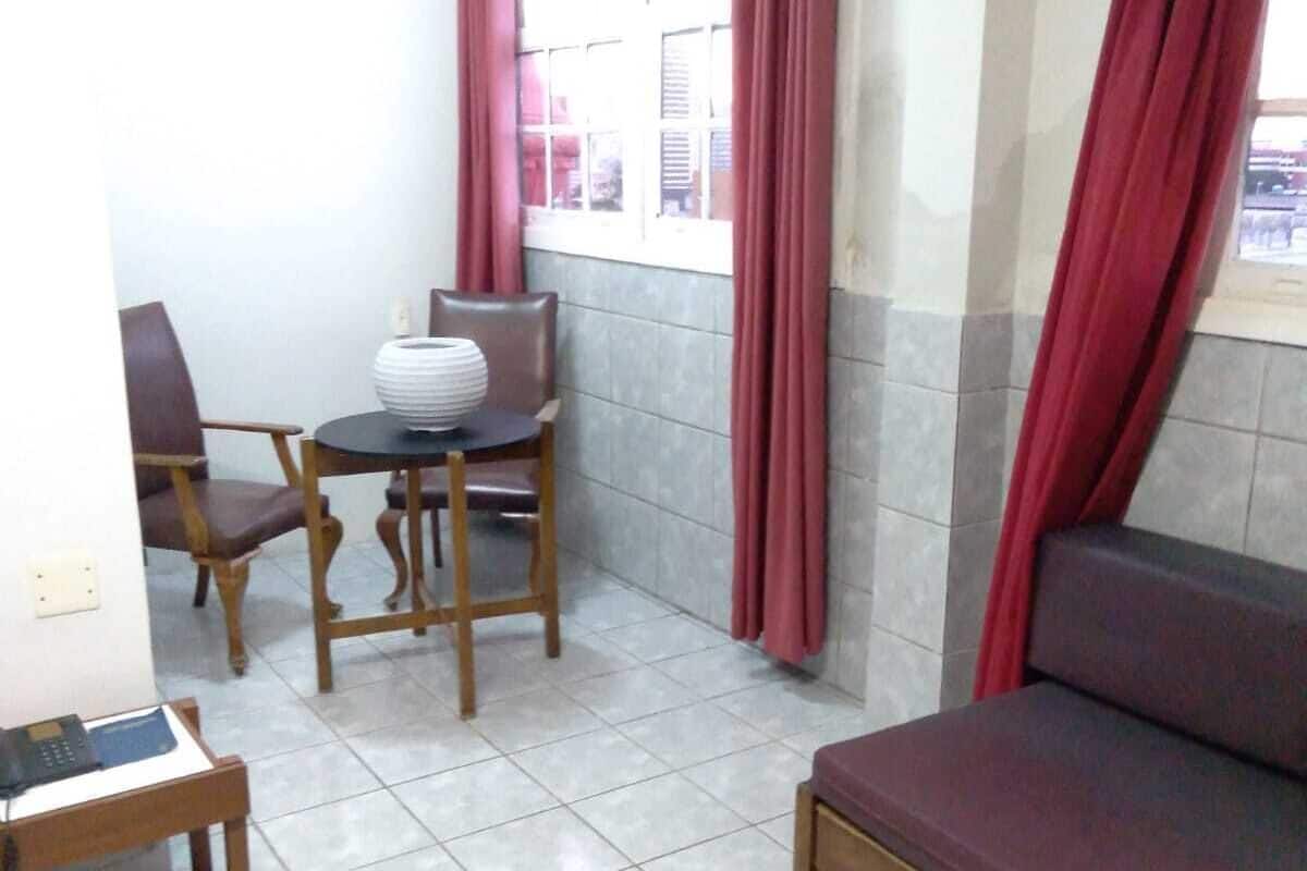 A small, tiled room with a sofa, a table with chairs, and a window with curtains.
