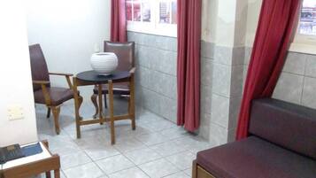 A small, tiled room with a sofa, a table with chairs, and a window with curtains.