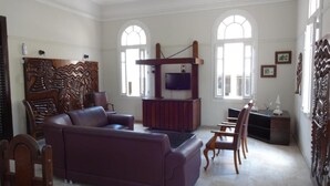 A spacious living room with a large purple sofa, wooden chairs, a wooden entertainment unit with a TV, and a decorative wall panel. - Hotel Central Recife (Recife)
