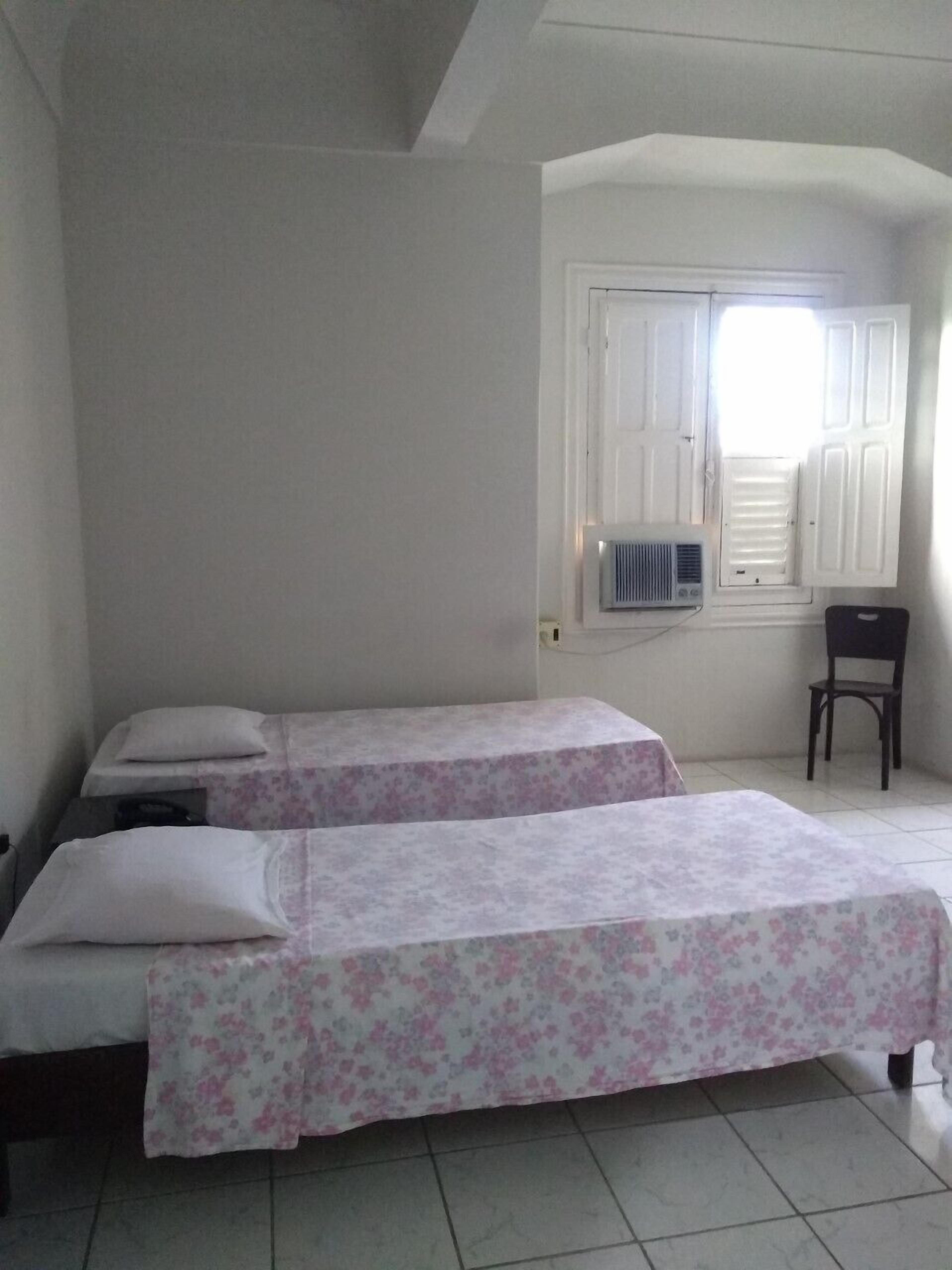 Una habitación con dos camas, una ventana con contraventanas, un radiador y una silla.
