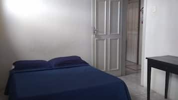 Un dormitorio con una cama, un escritorio y una puerta que da a otra habitación.