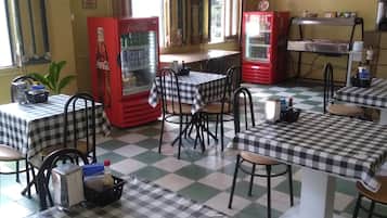 Un comedor con manteles a cuadros, refrigeradores rojos de Coca-Cola y un televisor en la pared.