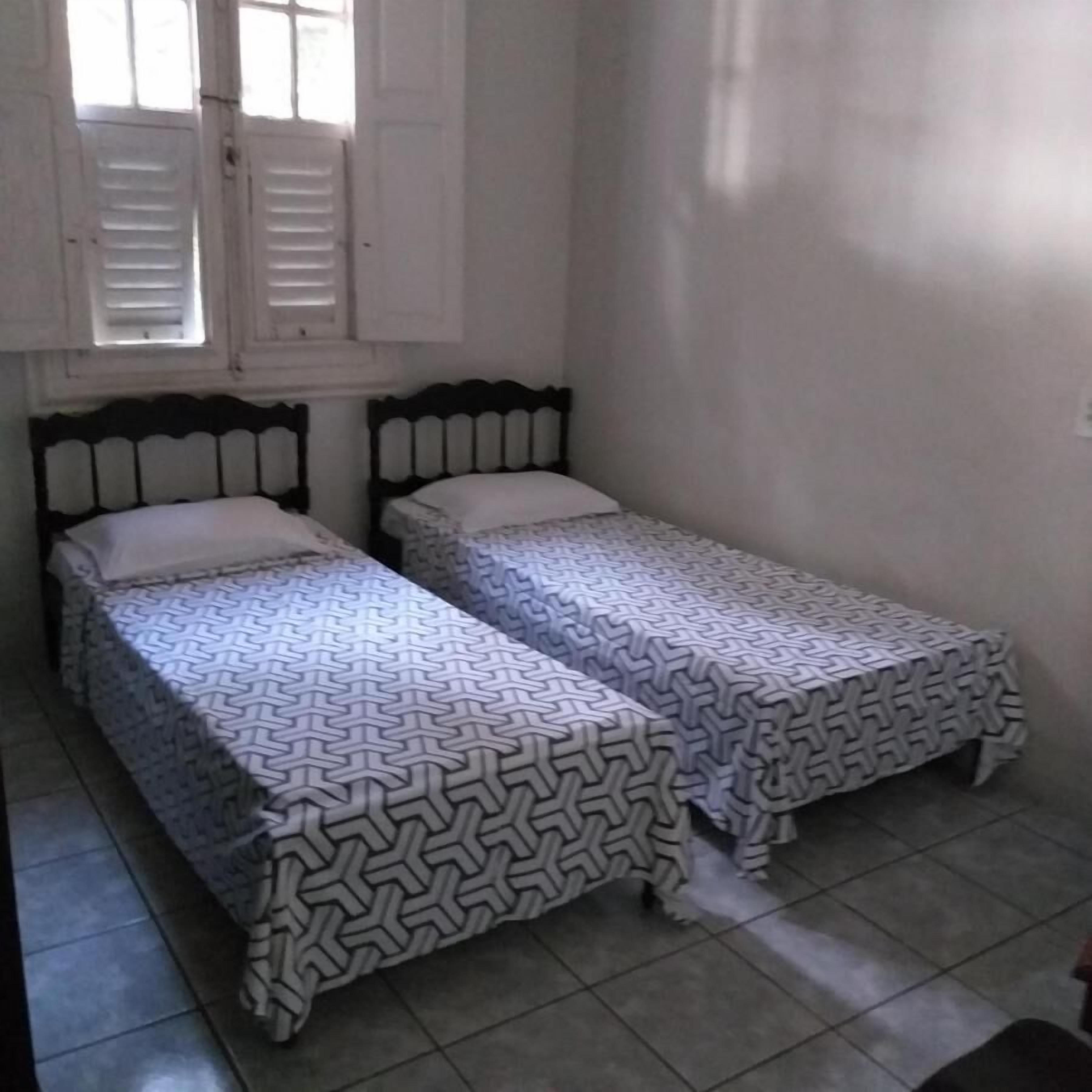 Una habitación pequeña y limpia con dos camas individuales, una ventana con persianas y suelo de baldosas.