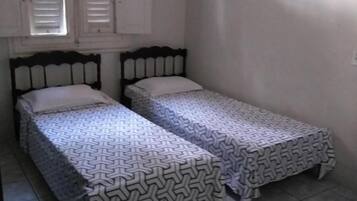 Una habitación pequeña y limpia con dos camas individuales, una ventana con persianas y suelo de baldosas.
