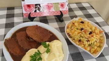 Una mesa con mantel a cuadros, un plato de carne con salsa y decoración, y un bol de arroz con verduras.