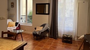 A living room with a sofa, a chair, a small table, and a window with a view of a balcony. - Quiet, cozy apartment on flower-filled courtyard in Paris. (Paris)