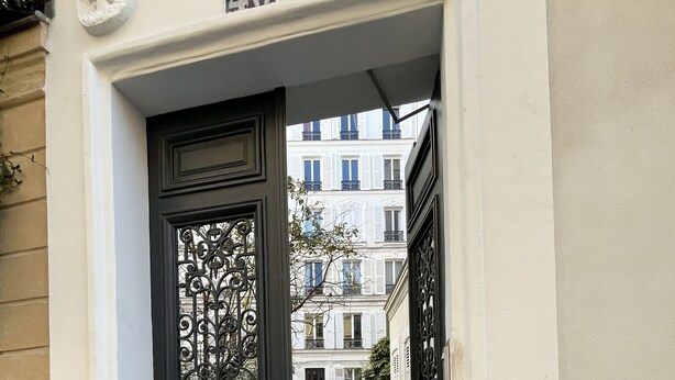 A black ornate door with a number '40' above it, leading to a narrow cobblestone street in a European-style building. - Quiet, cozy apartment on flower-filled courtyard in Paris. (Paris)
