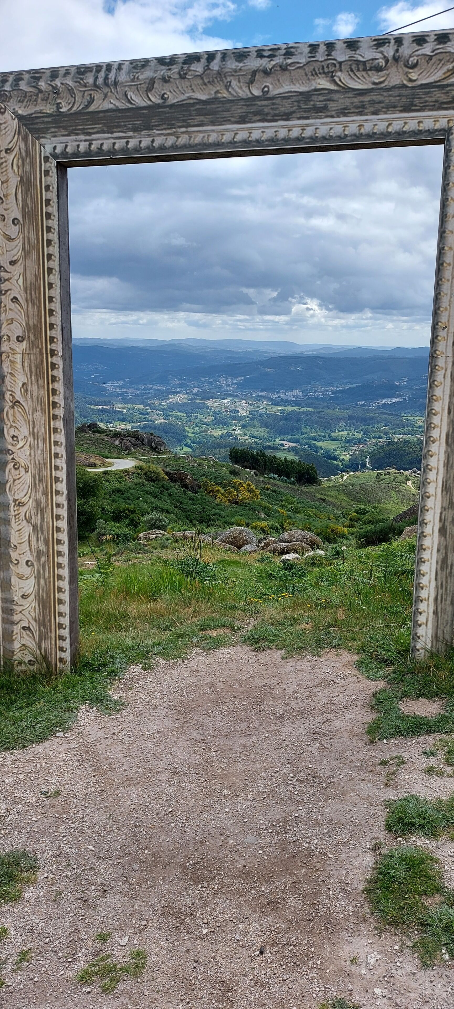 A rustic wooden frame with a view of a green landscape and distant hills.