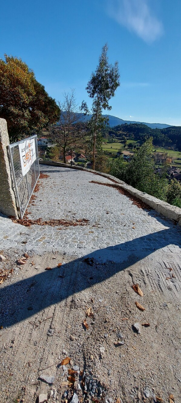 A paved pathway with a metal fence on one side and a view of a rural landscape with houses and trees in the distance.