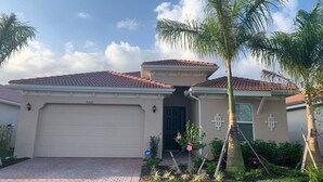 A single-story house with a red-tiled roof, beige exterior walls, and a garage door. - New Elegant Vacation Home in Fabulous Fort Myers (Fort Myers)