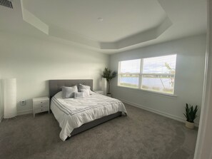 Ein Schlafzimmer mit einem Bett, einem Nachttisch, einer Topfpflanze und einem Fenster mit Blick auf ein Gewässer.