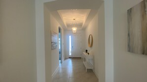 A hallway with a white door at the end, a bench, and a small table with a plant and candles. - New Elegant Vacation Home in Fabulous Fort Myers (Fort Myers)