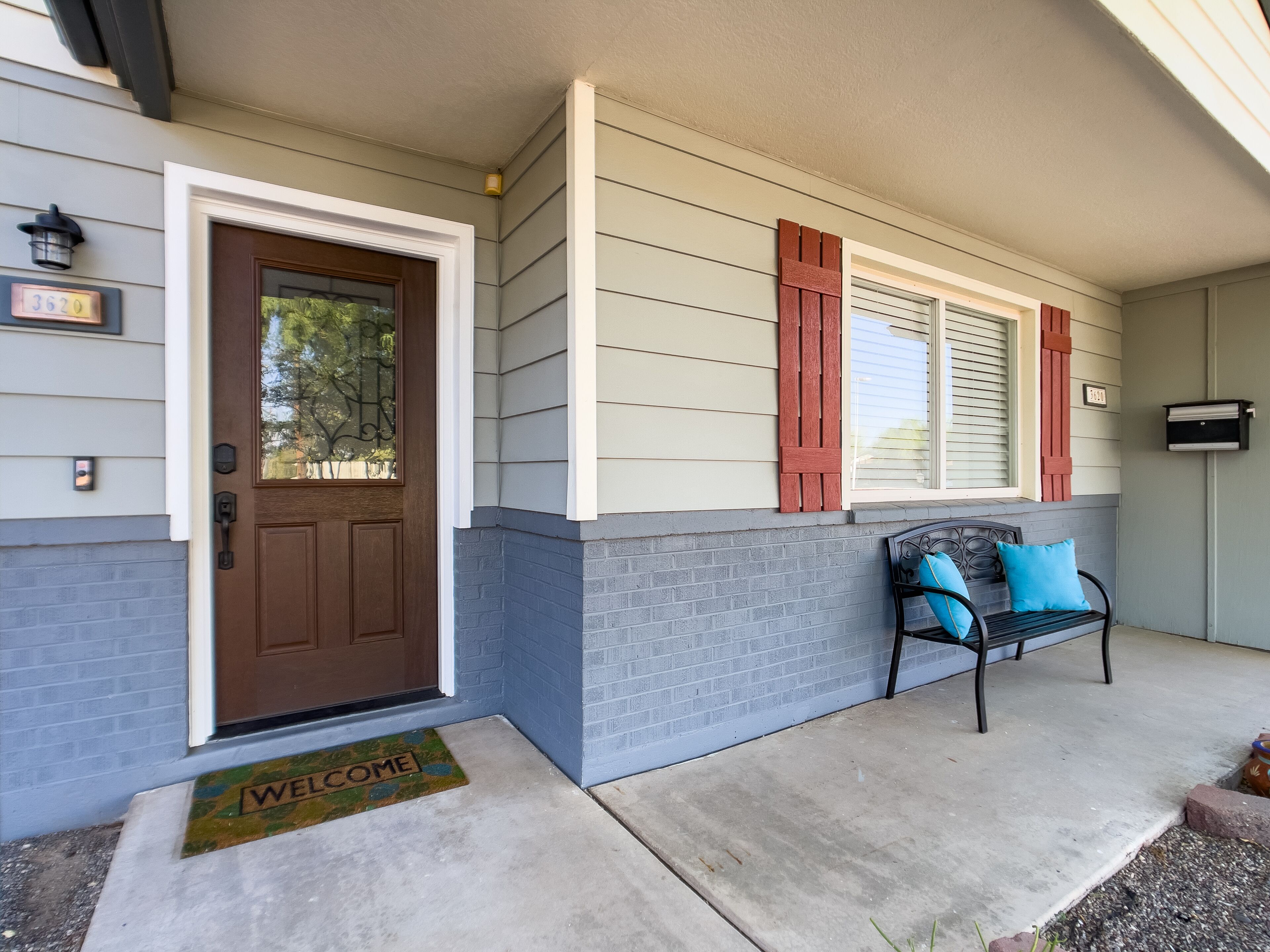 A house with a brown front door, a welcome mat, and a bench with blue cushions.