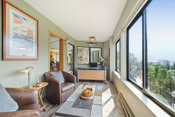 Relax in this stylish living room with a high ceiling and expansive views, featuring a comfortable sofa, a wooden coffee table, and a desk with a globe.