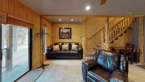 A cozy living room with a leather sofa, a wooden staircase, and a dining area. - Walk to Lifts | Wooded Area | Rustic Interior | French Henry B2 (Angel Fire)