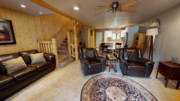 A spacious living room with a leather sofa, two leather armchairs, a patterned rug, and a wooden staircase leading to an upper level. - Walk to Lifts | Wooded Area | Rustic Interior | French Henry B2 (Angel Fire)
