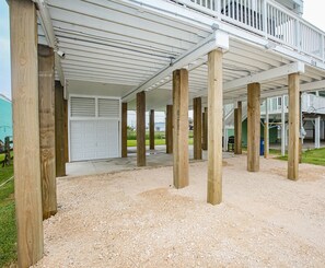 A covered outdoor area with wooden pillars, a white garage door, and a staircase leading to a second level. - Kalm by the Beach - Ocean View - Sleeps 14 (Surfside Beach)