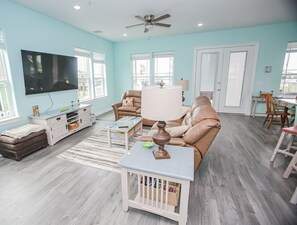 A spacious living room with a large flat-screen TV, comfortable seating, and a ceiling fan. - Kalm by the Beach - Ocean View - Sleeps 14 (Surfside Beach)