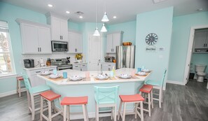 A modern kitchen with white cabinets, a central island with stools, and a clock on the wall. - Kalm by the Beach - Ocean View - Sleeps 14 (Surfside Beach)