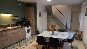 A compact kitchen with a washing machine, a dining table with chairs, and a staircase leading to another level. - La Forge, house for 6 in the heart of Barfleur, with private parking lot (Barfleur)
