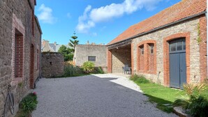 A courtyard with a gravel path, stone walls, and a brick building with a door and window. - La Forge, house for 6 in the heart of Barfleur, with private parking lot (Barfleur)