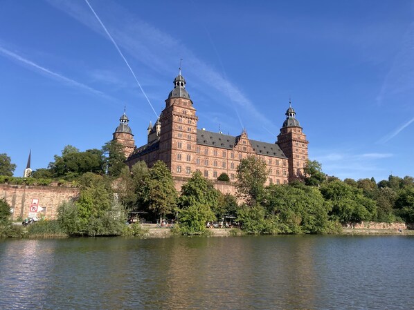 A historic building with multiple towers and a large courtyard, surrounded by lush greenery and a body of water.