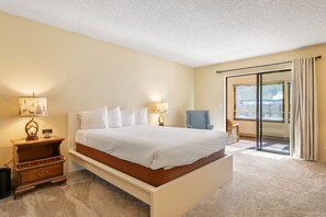 Relax in a spacious room with a large bed, wicker chair, and sliding glass door leading to an outdoor area.