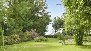 A lush garden with a bench and chairs, surrounded by dense foliage and flowering plants. - 2 bedroom accommodation in Narberth (Narberth)