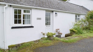 A white cottage with a stone roof, a sign reading "Stoneyford Cottage," and a small garden with potted plants and a stone feature. - 2 bedroom accommodation in Narberth (Narberth)