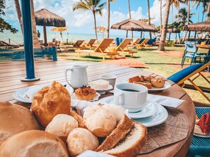 Une table garnie de nourriture et de boissons, des chaises de plage et des parasols, le tout dans un cadre tropical.