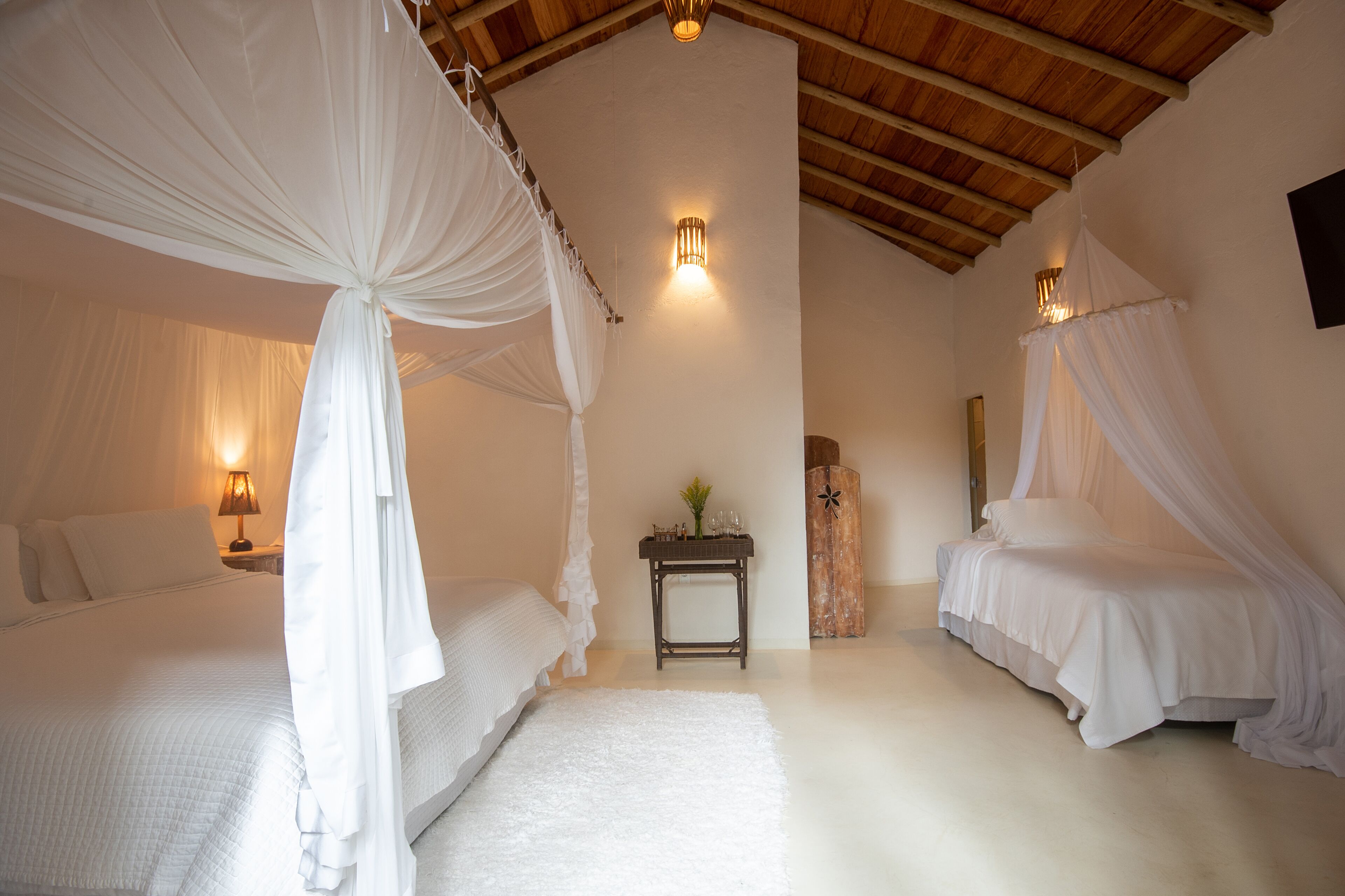 A bedroom with two beds, each with a canopy, a small table with a lamp, and a wall-mounted light fixture.