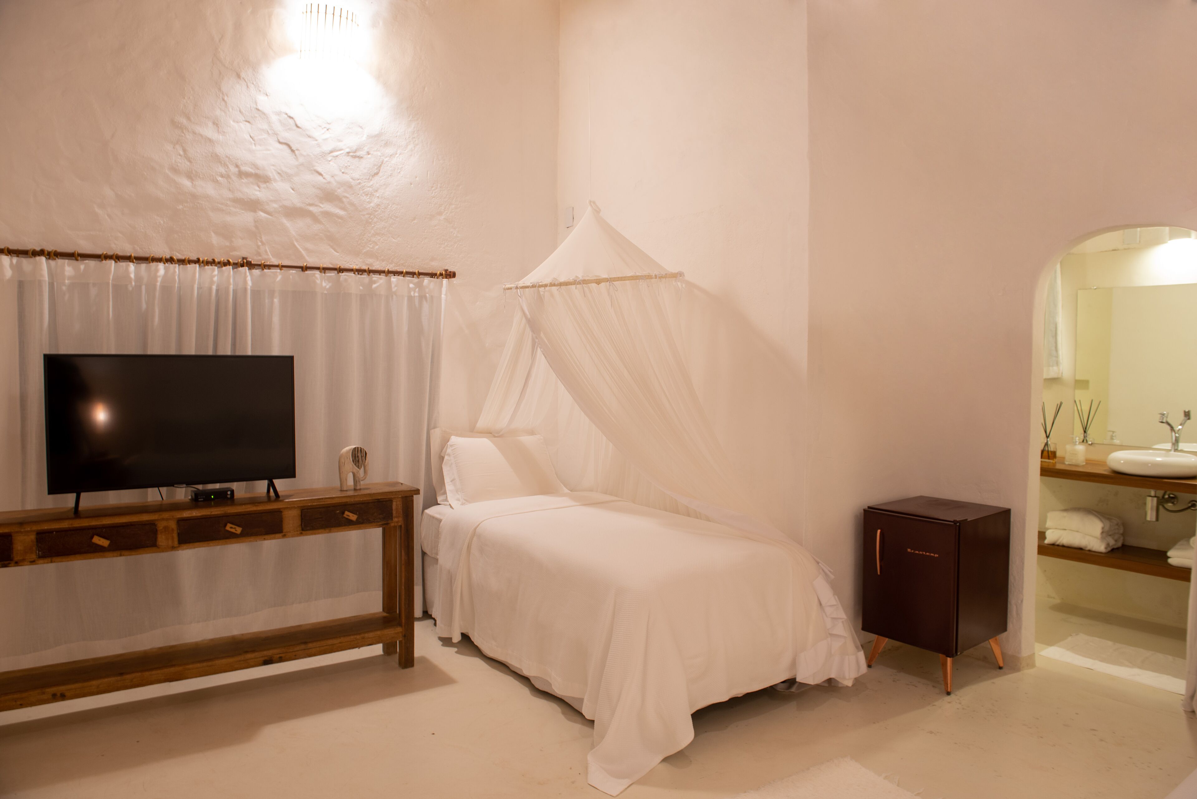A bedroom with a bed, a TV, a bedside cabinet, and a bathroom with a sink and mirror.