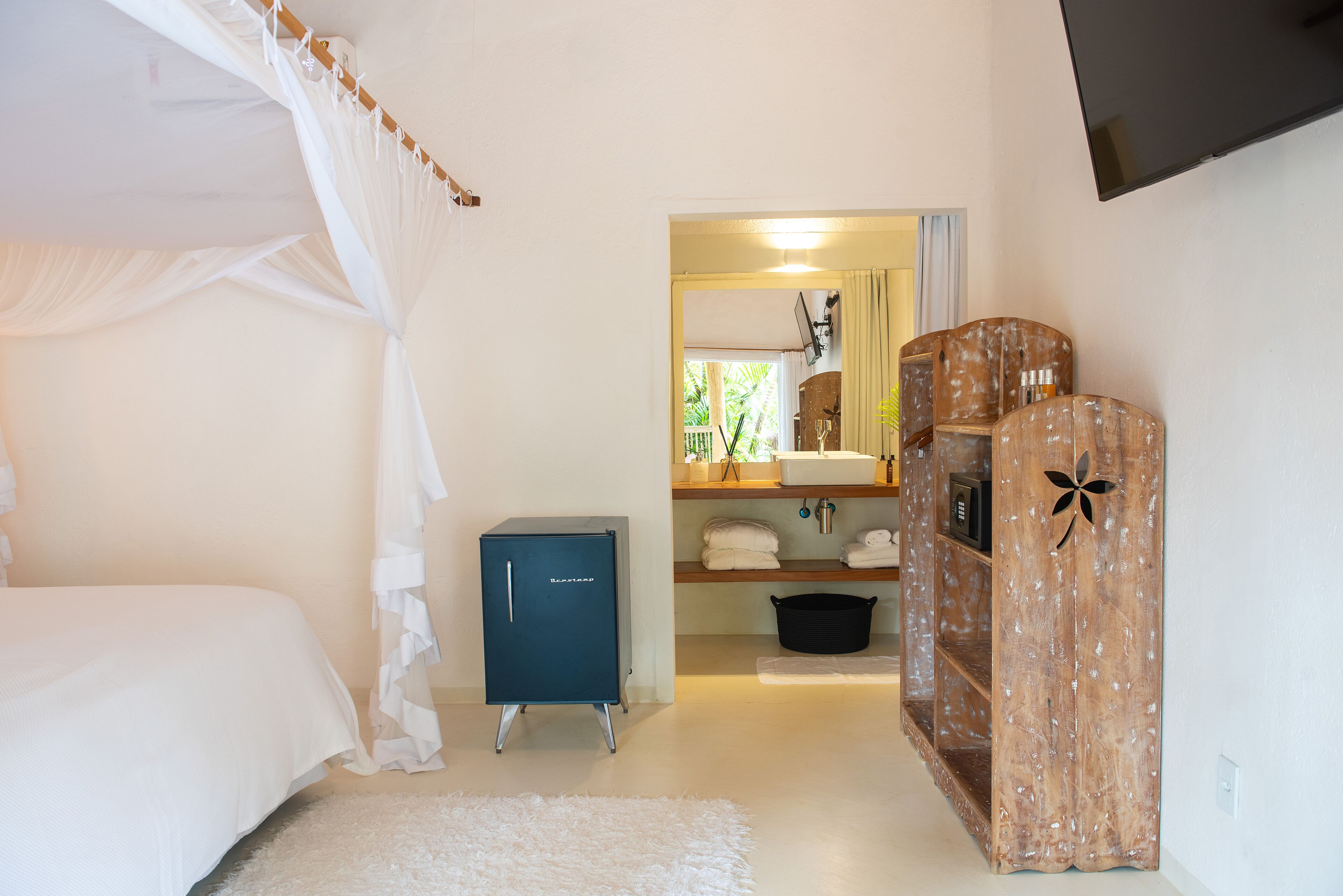 A bedroom with a bed, a wardrobe, a small cabinet, and a television mounted on the wall.