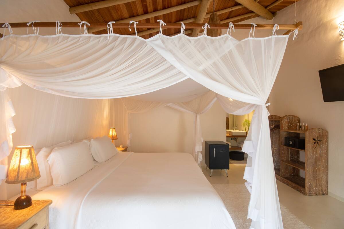 Een slaapkamer met een hemelbed, een bedlampje en een houten kast.