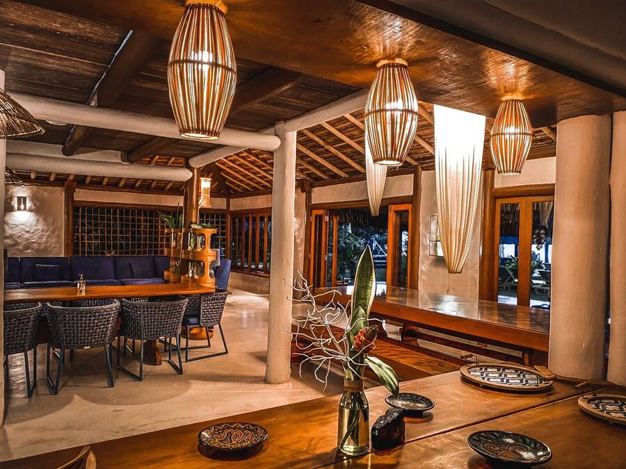 Un comedor amplio con una mesa de madera, sillas de mimbre y lámparas colgantes.