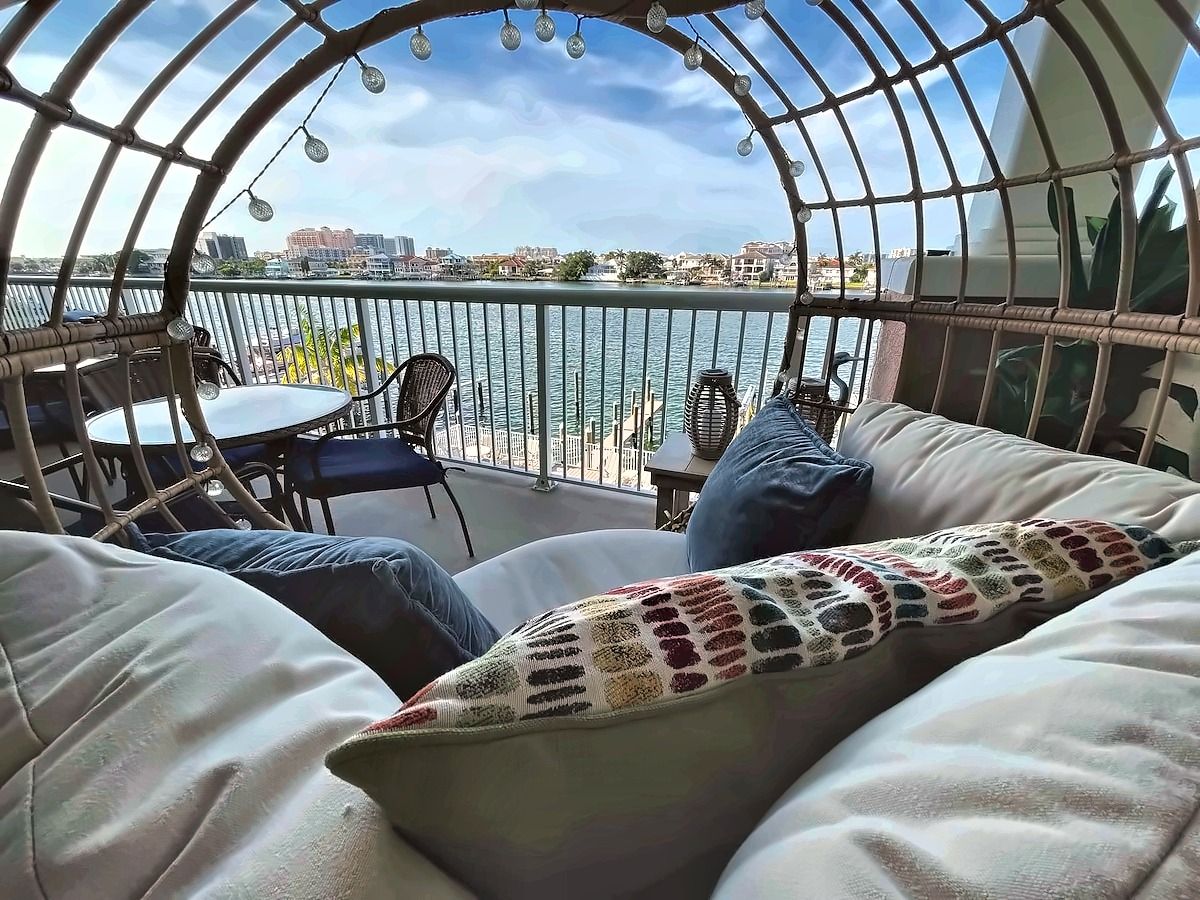 A cozy balcony with a view of the water, wicker furniture, and a crocheted throw.
