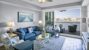 Una sala de estar moderna con un sofá, sillones y una mesa de centro. Hay un balcón con mobiliario exterior y vistas a la ciudad.