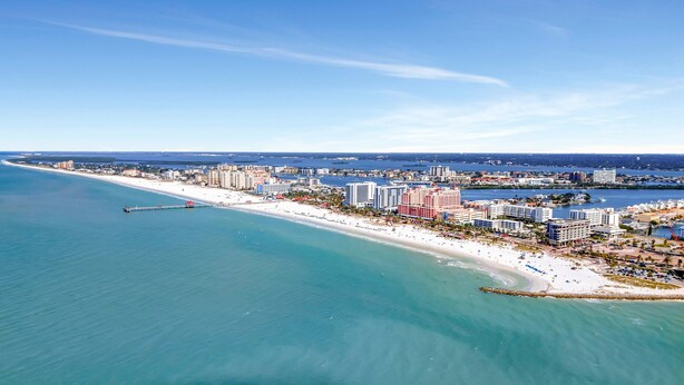 Vista aérea de una ciudad costera con una extensa playa de arena, varios hoteles de gran altura y un puerto deportivo.