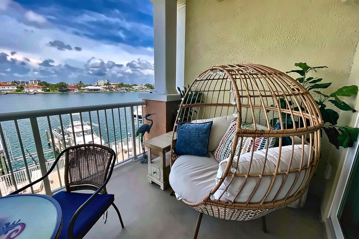 Un balcón con una silla de mimbre, una mesita y vistas al agua.