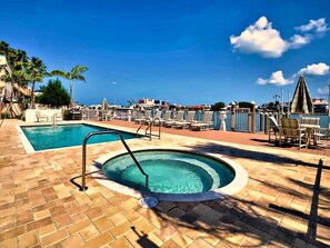 A swimming pool area with a hot tub, lounge chairs, and a view of the city skyline.