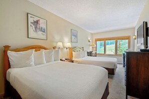Two large beds with white linens, a flat-screen TV, and a desk with a lamp are featured in this room.