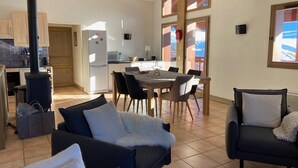 A modern living room with a fireplace, a dining area with a table and chairs, and a kitchen with a stove and refrigerator. - B306 - 79 m2 - 4P - 8 pers (Prapoutel)