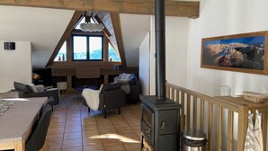 A cozy loft-style living room with a fireplace, wooden beams, a dining area, and a large window offering a mountain view. - B306 - 79 m2 - 4P - 8 pers (Prapoutel)