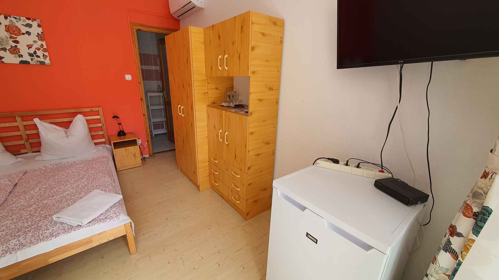 A bedroom with a bed, a wardrobe, a television, and a small refrigerator.