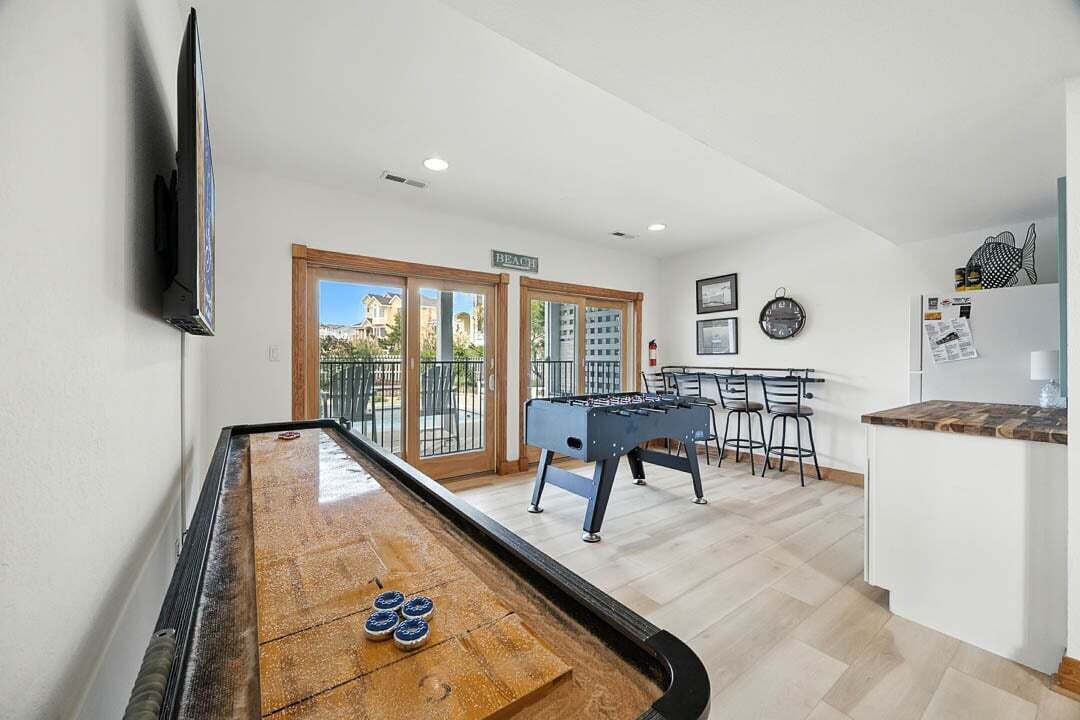 A pool table, foosball table, and a bar area with a refrigerator and chairs.